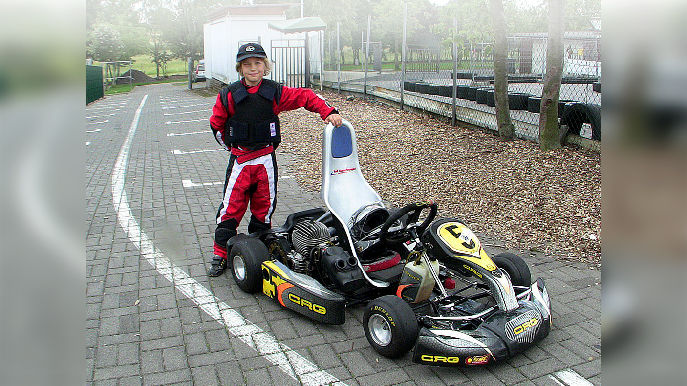 7-jähriger Kartfahrer Denis Robin Wolf im Rennanzug, stolz neben seinem CRG Rennkart stehend