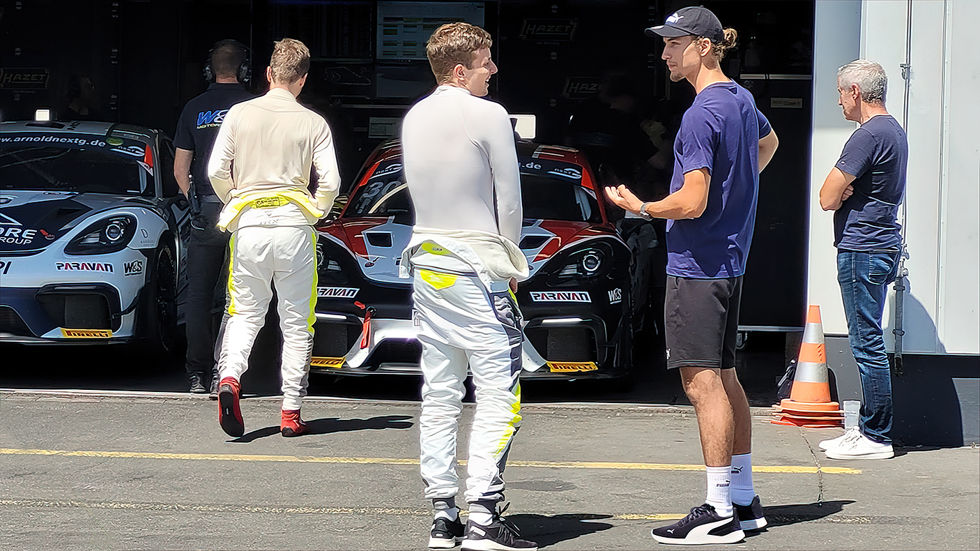20-jähriger Rennfahrer Denis Robin Wolf auf dem Nürburgring- vor der Box eines befreundeten Rennfahrers und dessem Porsche GT4 Rennwagen, sich im Gespräch befindend 